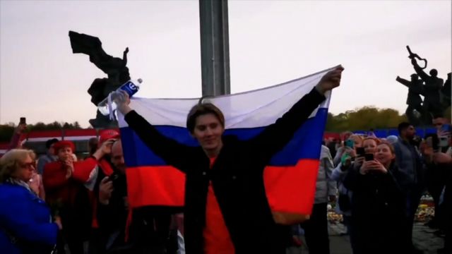 Alexander Dubyako vẫy cờ Nga cho đám đông tụ tập trước đài tưởng niệm chiến tranh của Riga vào ngày 10 tháng 5 năm 2022
